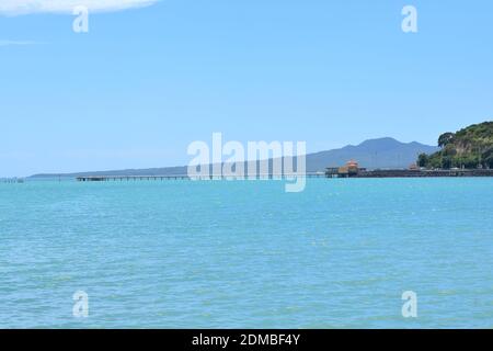 Vista del Molo della Baia di Okahu e del Ponte con Vista Mare Tamaki Drive con Rangitoto dormiente vulcano isola in background Foto Stock