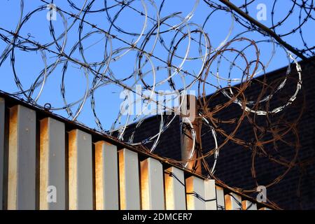 Several layers of razor wire on top of a metal fence with a blue sky background. Stock Photo