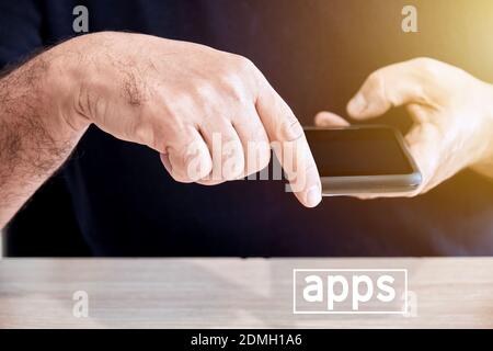 Il maschio tiene in mano un telefono cellulare o uno smartphone con il dito rivolto verso la parola apps. Per scaricare o utilizzare le applicazioni in Smart Foto Stock