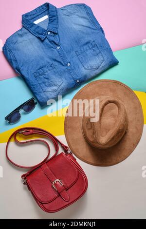 Abbigliamento e accessori moda donna. Camicia in denim, cappello in feltro, borsa in pelle, occhiali da sole, disposizione su sfondo colorato. Vista dall'alto, disposizione piatta Foto Stock