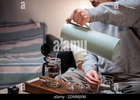 Un uomo attende gli ospiti e prepara un autentico tè cinese utilizzando un kit per la cerimonia del tè. Eroga le foglie di tè crudo mature in acqua calda secondo le istruzioni del maestro del tè Foto Stock