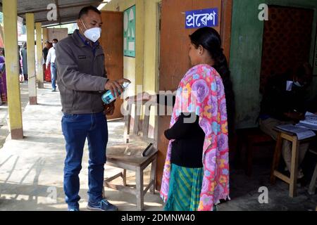 Nagaon, Assam, India - 17 dicembre 2020: Un operatore sanitario che spruzza tutti gli elettori in coda a causa della pandemia di Covid - 19 in una stazione di polling durante l'elezione del Consiglio autonomo di Tiwa nel villaggio di Kachamari nel distretto di Nagaon ad Assam, India. Credit: Dita TALUKDAR/Alamy Live News Foto Stock