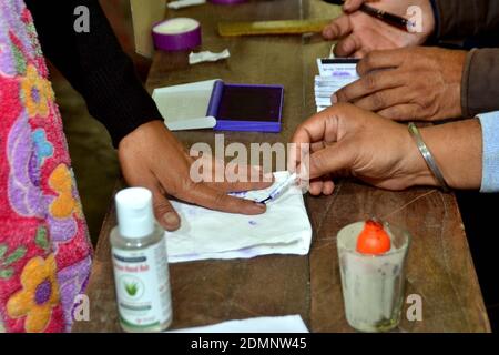 Nagaon, Assam, India - 17 dicembre 2020: Un funzionario elettorale impegnato a dare il segno sul dito di un elettore in una stazione di polling durante le elezioni del Consiglio autonomo di Tiwa nel villaggio di Kachamari nel distretto di Nagaon ad Assam, India. Credit: Dita TALUKDAR/Alamy Live News Foto Stock