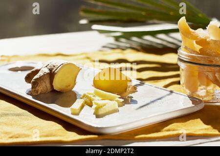 Radice di zenzero fresco e fette di zenzero candito in un vaso di vetro sul tavolo con un'ombra di foglia di palma. Frutta orientale disidratata. Dolci sani. Antioxida Foto Stock