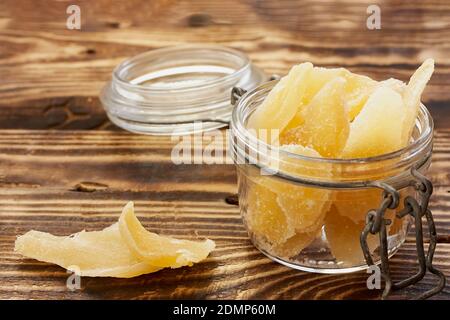 Fette di zenzero candito in un vaso di vetro su un tavolo di legno. Frutta orientale disidratata. Dolci sani. Antiossidanti. Foto Stock