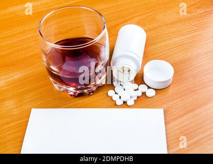 Bicchiere del Whiskey con pillole e carta vuota Nella pagina di primo piano del tavolo Foto Stock