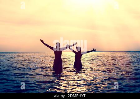 Toned Photo of Happy Couple Silhouette with Hands Up in the Water Stock Photo