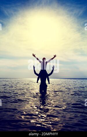 Toned Photo of Happy Couple Silhouette with Hands Up in the Water Stock Photo