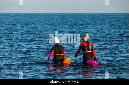 Due persone che entrano nel Mare del Nord circa per andare a nuotare, indossando mute, Kirkcaldy , Fife, Scozia Foto Stock