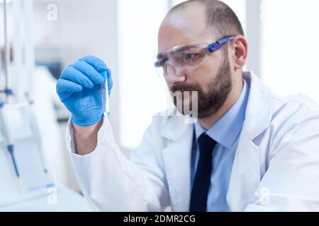 Scienziato concentrato nella conduzione laboratosa del reseach dei campioni. Ricercatore in laboratorio sterile biotecnologico che tiene analisi in tubo indossando guanti e occhiali di protezione. Foto Stock