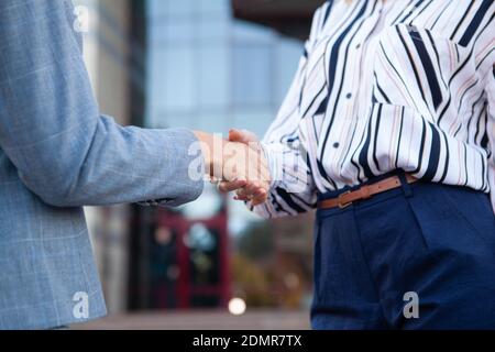 Primo piano corto di due donne d'affari che scuotono le mani. Stretta di mano di due donne, business building sullo sfondo Foto Stock
