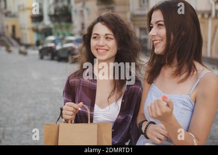 Felici le giovani amiche che ridono, camminano per le strade della città, trasportano borse per lo shopping. Vacanza, avvistamento, concetto di viaggio Foto Stock