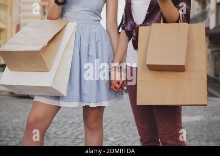 Ripresa tagliata di due donne che trasportano borse per la spesa, tenendo le mani mentre si cammina. Due amiche che camminano in città tenendo le mani Foto Stock
