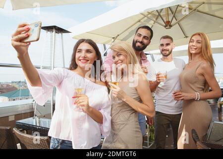 Group of friends taking selfies on a smart phone together during rooftop party Foto Stock