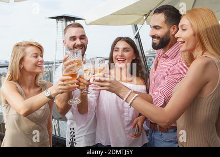 Felici i giovani che gridano con gioia, brindisi con i loro bicchieri, festeggiando su una festa sul tetto Foto Stock