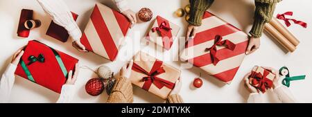 Disposizione piatta delle mani femminili che tengono scatole di regalo con carta da imballaggio, baubles colorati, palle, nastri su fondo bianco semplice, vista dall'alto. Biglietto d'auguri alla moda per le vacanze di Natale, striscione Foto Stock