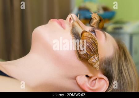 Una grande lumaca Akhatina striscia sul volto di una giovane donna e ringiovanisce la sua pelle. Il concetto di cura insolito e ringiovanimento della pelle della f Foto Stock