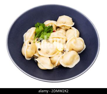 Pelmeni cotti (gnocchi russi ripieni di carne tritata) con burro e decorato con foglie di prezzemolo verde in nero ciotola isolata su sfondo bianco Foto Stock