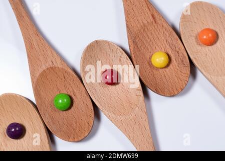 Cinque cucchiai di legno su sfondo bianco con caramelle colorate Foto Stock