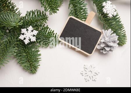 Composizione natalizia con rami di abete verde, decorazioni in legno bianco e cono di fiocchi di neve su fondo di legno bianco, con copyspace Foto Stock