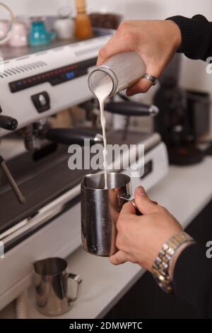Un barista maschio che versa latte in un punto verticale tagliato caraffa per la schiuma Foto Stock