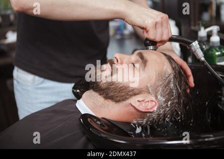 Uomo bearded godendo del lavaggio dei capelli da barbiere professionale al salone Foto Stock