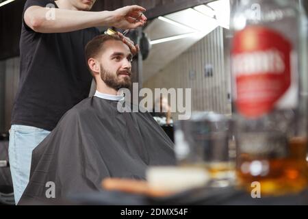 Bell'uomo sopportato sorridendo mentre ottiene un nuovo taglio di capelli a. barbiere locale Foto Stock