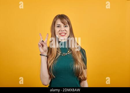 Alzando due dita sulla mano è mostra la lotta di forza di pace o simbolo di vittoria e lettera v in lingua dei segni. Il gesto numero 2, sorride splendidamente, mostrando. Giovane donna attraente Foto Stock