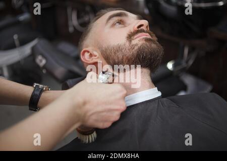 Immagine ritagliata di un barbiere utilizzando il regolacapelli elettrico sul barba del cliente maschile Foto Stock