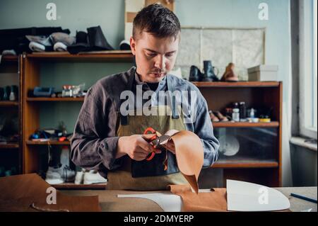 Un giovane ragazzo di talento aiuta suo padre nel commercio di famiglia, taglia fuori gli sbozzi per le scarpe dalla pelle. Foto Stock