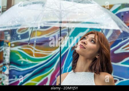 Una donna cinese asiatica che tiene un ombrello trasparente in caduta di luce pioggia Foto Stock