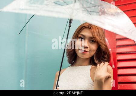 Una donna cinese asiatica che tiene un ombrello trasparente in caduta di luce pioggia Foto Stock