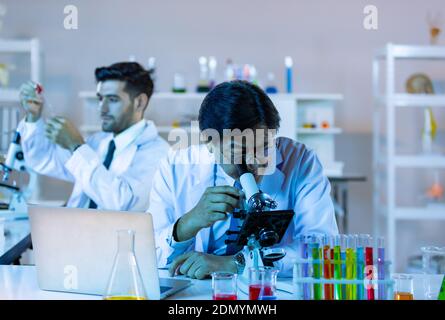 Il ricercatore di biotecnologia microbiologa o il team di lavoratori medici osservano il microscopio in laboratorio per la ricerca di dati chimici da parte di scienziati asiatici. Foto Stock