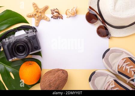 Bianco di carta, foglia di monstera, macchina fotografica, sneakers e accessori estivi su sfondo giallo pastello - immagine Foto Stock