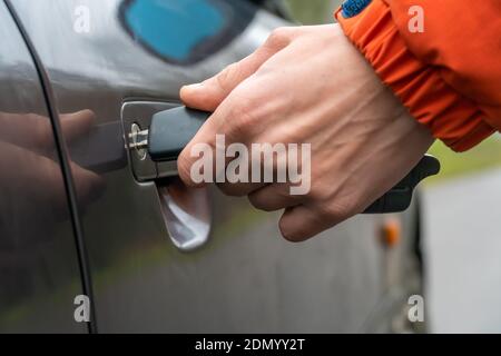 Primo piano della mano sinistra di un uomo in una giacca arancione inserendo una chiave nella serratura della porta dell'auto. Foto Stock