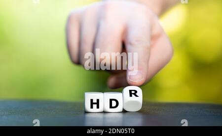 Simbolo di un televisore HDR (High Dynamic Range). La mano trasforma i dadi e cambia l'espressione "HD" in "HDR". Foto Stock
