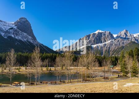Quarry Lake park lakeshore in late autumn season sunny day morning. Snow capped Mount Rundle and Mount Lawrence Grassi Ha Ling Peak in with blue sky Stock Photo