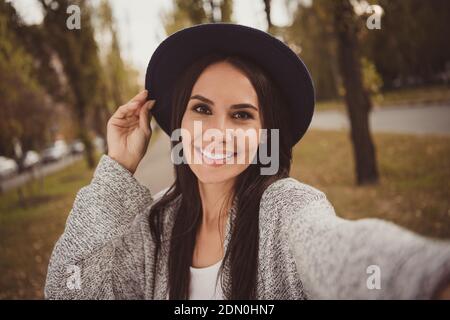 Ritratto fotografico di bruna felice in cappello nero prendendo selfie all'esterno sorridente indossando abiti grigi Foto Stock