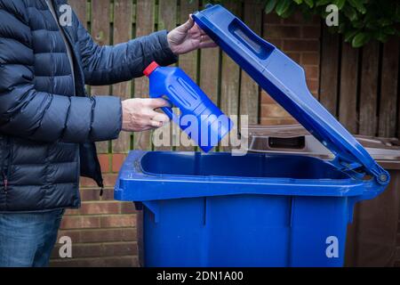 Un uomo responsabile che inserisce una bottiglia di plastica blu in un contenitore per riciclaggio a lato del marciapiede pronto per la raccolta e il riciclaggio da parte di Consiglio nel Regno Unito Foto Stock
