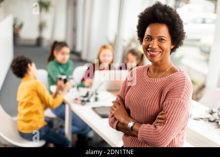 Smily African American insegnante di scienza femminile con gruppo di bambini programmazione di giocattoli e robot elettrici in classe robotica Foto Stock