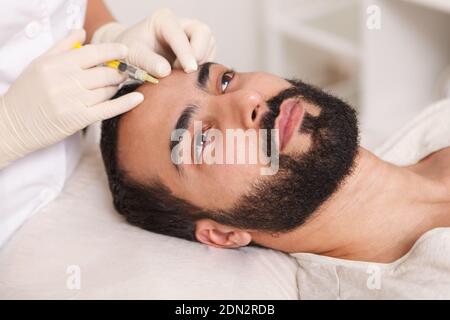 Uomo bearded ottenere iniezioni di riempimento facciale da parte del cosmetologo Foto Stock