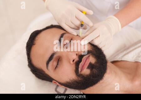 Vista dall'alto in primo piano di un uomo bearded che ottiene anti-invecchiamento iniezioni di riempitivo presso la clinica di bellezza Foto Stock