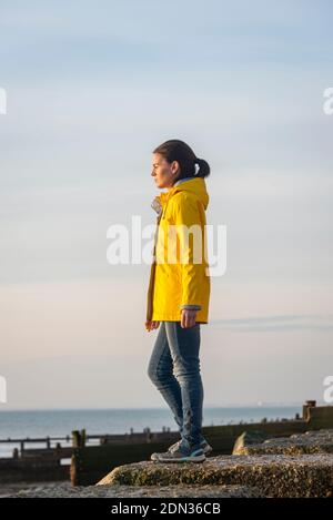 Donna matura che indossa una giacca gialla, guardando verso il mare. Concetto unico. Foto Stock
