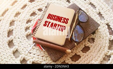 Avvio aziendale scritto su un notebook con penna, occhiali su panno a crochet. Nuovo concetto di business case di successo Foto Stock