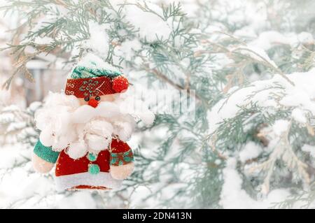 simpatico giocattolo imbottito babbo natale sullo sfondo di rami innevati dell'albero di natale. Bambola Babbo Natale. Spazio copia. Foto Stock