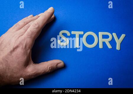 Mano umana accanto alla parola Storia scritta con lettere di plastica su sfondo di carta blu, concetto Foto Stock