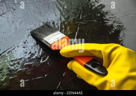 Mano con spazzola in un guanto di gomma giallo, vernici con vernice nera. Il concetto di design creativo Foto Stock