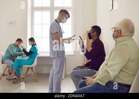 Preoccupato giovane uomo in maschera di faccia che chiede al medico una domanda in attesa di ricevere il vaccino Foto Stock
