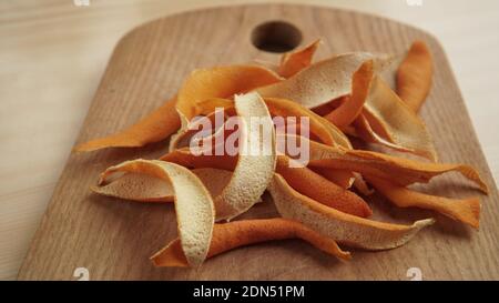Le bucce aranciate su un piano di cottura in legno in una vista ravvicinata. Un modo per aggiungere sapore al pasto. Struttura di spezie di frutta secca. Sapori naturali del cibo Foto Stock