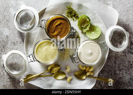 diversi tipi di salse in vasetti di vetro. con pistacchi, cashews e vegan mayo su uno sfondo di pietra Foto Stock